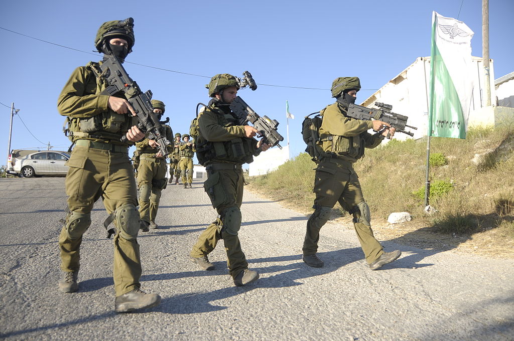Grupo de soldados das Forças de Defesa de Israel em ação. Em primeiro plano, três homens fardados e com armas.