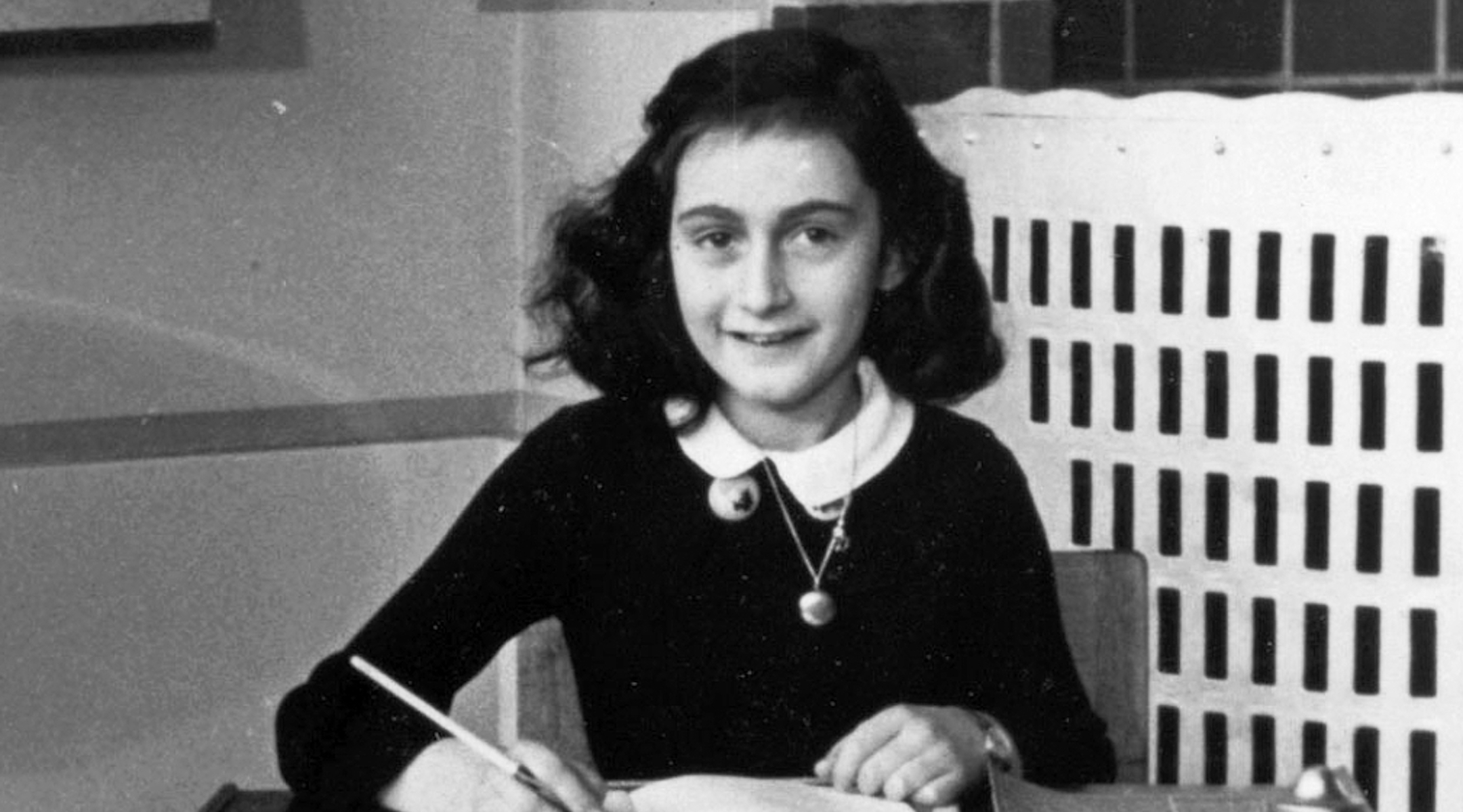 foto tradicional de Anne Frank sentada em mesa com caderno e livros